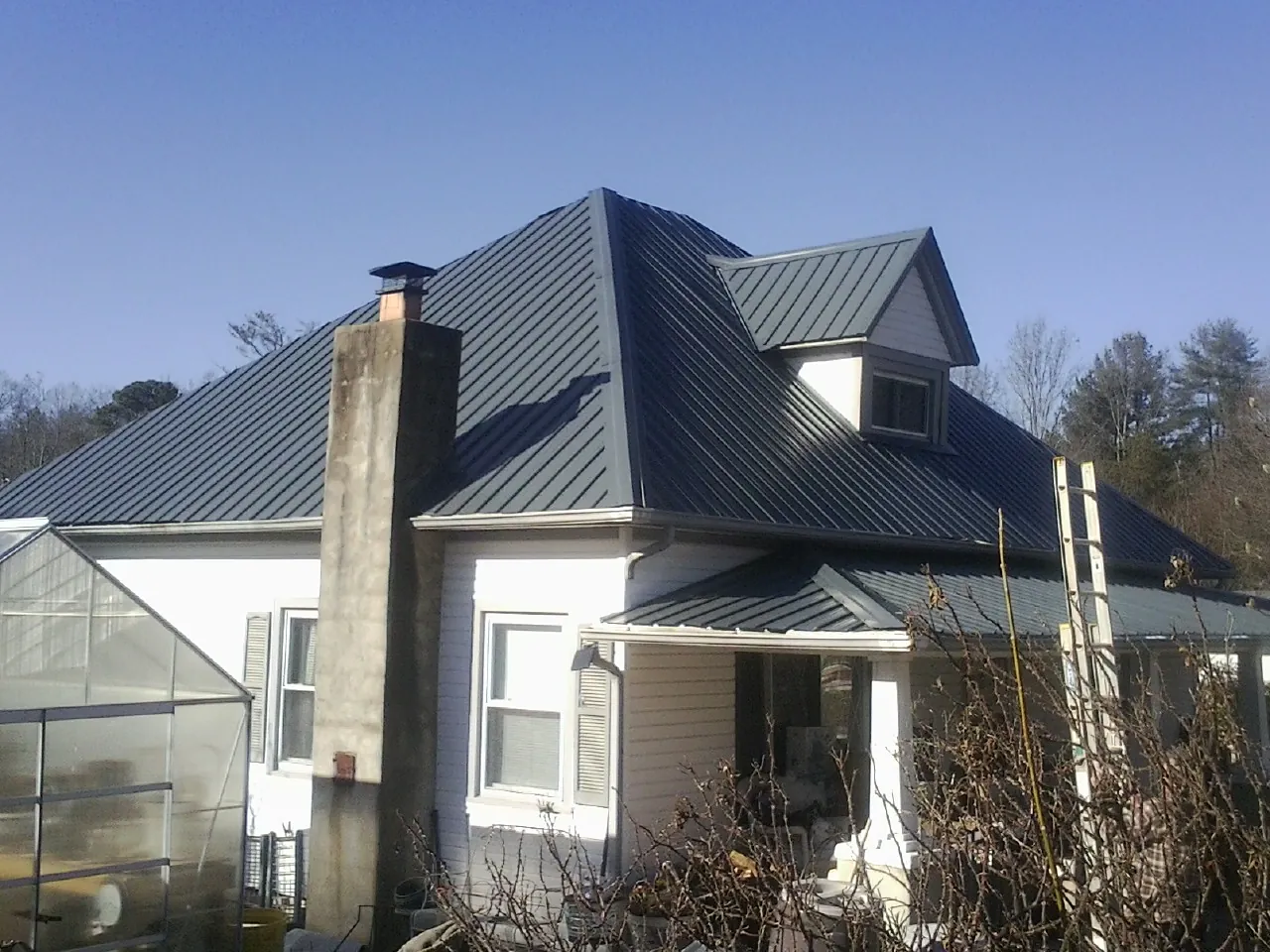 Dark blue standing seam metal roof on a white farmhouse with dormer — Slate & Tile Roof Repair by Roofing Brothers in Long Eddy