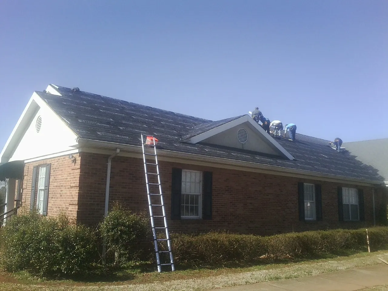 Crew tearing shingles off a brick ranch roof with a ladder set — Emergency Roof Repair work by our crew in Long Eddy