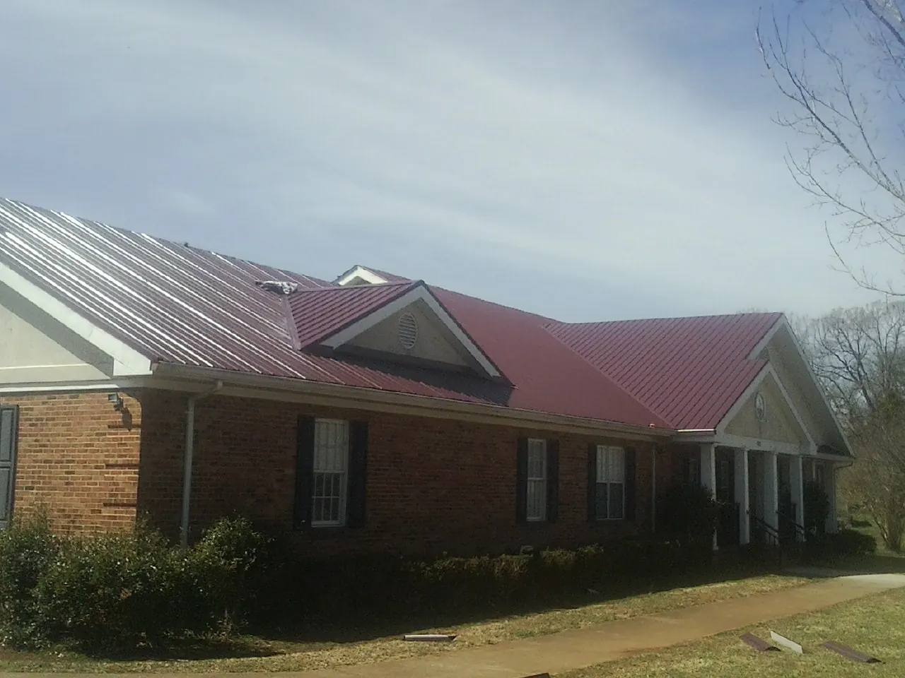 Red metal roof with gabled entries on a long brick building, from a Hail Damage Roof Repair job in Long Eddy