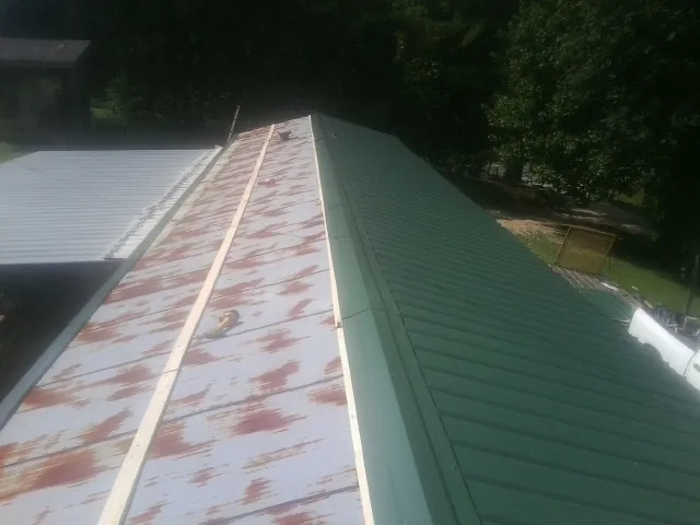 Old rusted panels beside newly installed green metal roofing — Wind Damage Roof Repair by Roofing Brothers in Long Eddy