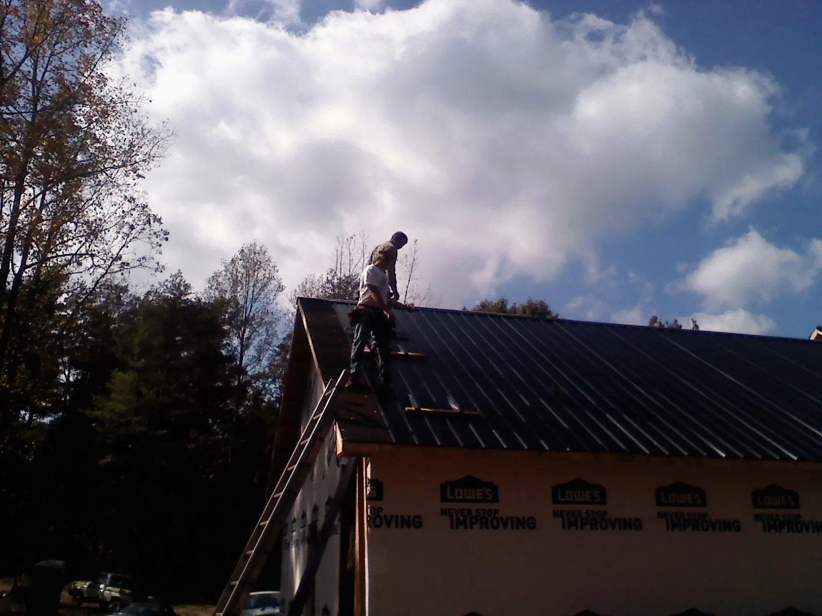 Roofer fastening dark metal panels high against a cloudy sky, from a Roof Inspection job in Long Eddy