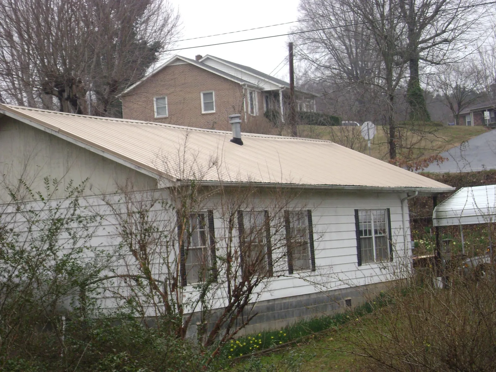 Tan metal roof on a white sided house set into a hillside — Commercial Roofing by Roofing Brothers in Long Eddy